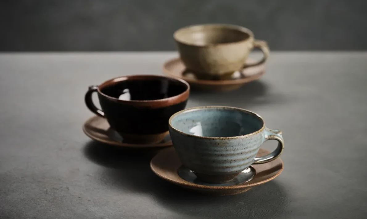 Three hand-thrown stoneware cups and saucers with blue, black and olive glazes